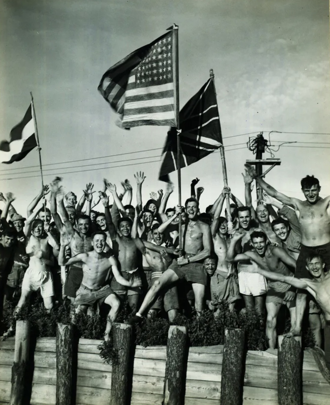 Gaunt Allied prisoners of war, waving flags of the United States, Great Britain, and Holland at Aomori camp near Yokohama, Japan, cheer rescuers from the U.S. Navy 